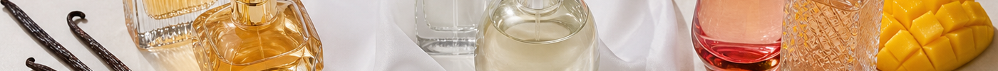 Perfume bottles styled with vanilla pods, soft white musk elements, and mixed fruits on a neutral surface.