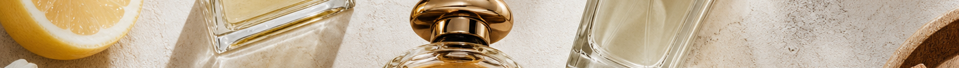 Several elegant perfume bottles arranged with citrus slices, white flowers, and wood accents on a light stone surface