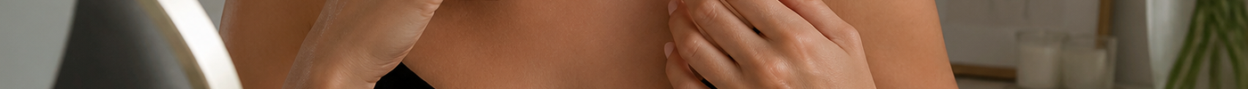 Person applying perfume to neck after moisturizing skin at a vanity.